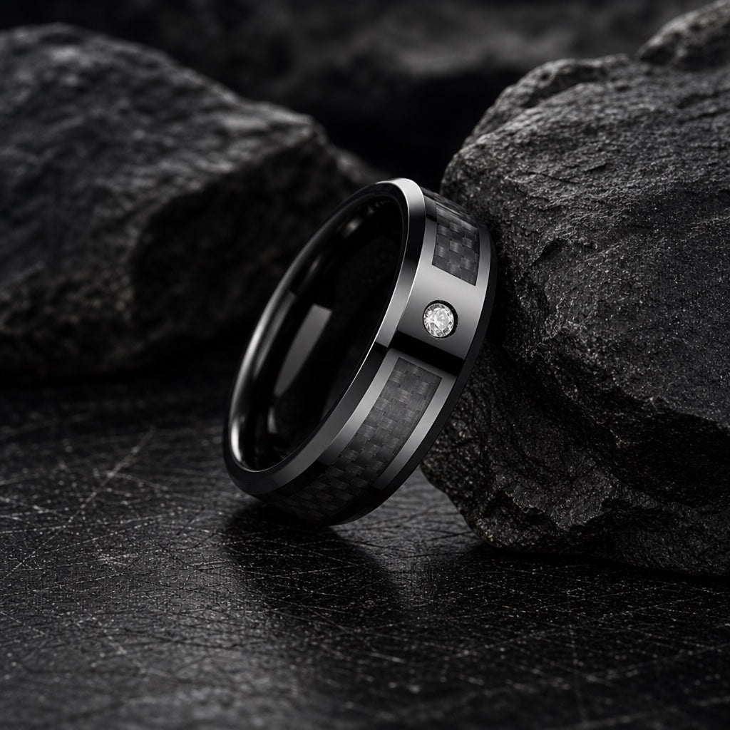 The Agile ring resting against dark charcoal rock, black tungsten body, bevelled edges and centred carbon fibre fully readable