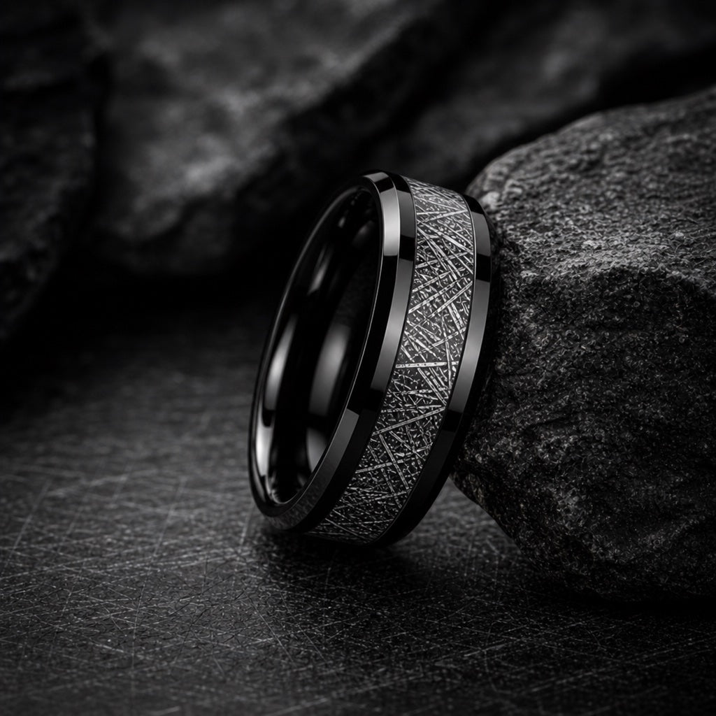 The Astro ring resting against dark rock, showing its black tungsten body