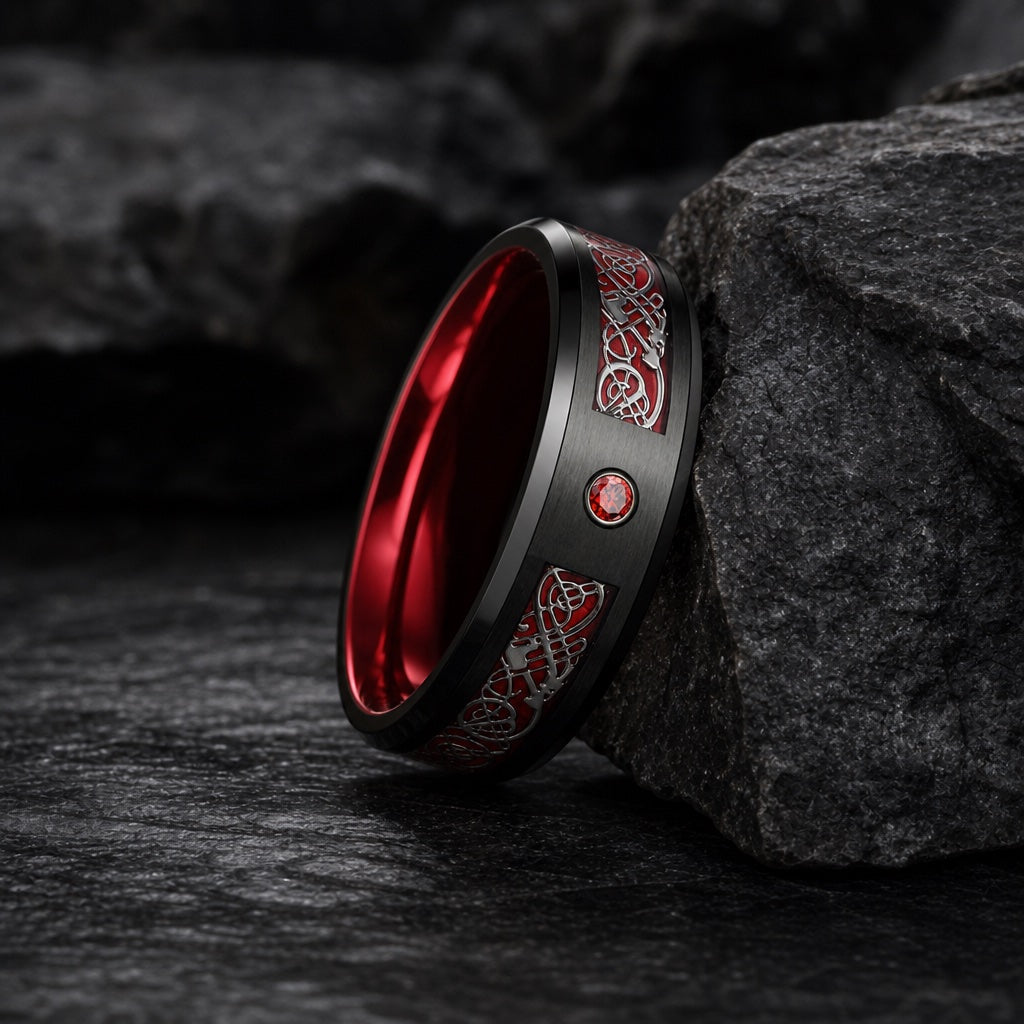 The Cardinal ring resting against dark charcoal rock, brushed black body, red Celtic channel and flush red centre stone visible