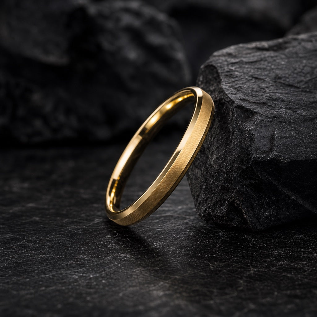 The Flare ring resting against dark charcoal rock, solid yellow gold and bevelled edges visible