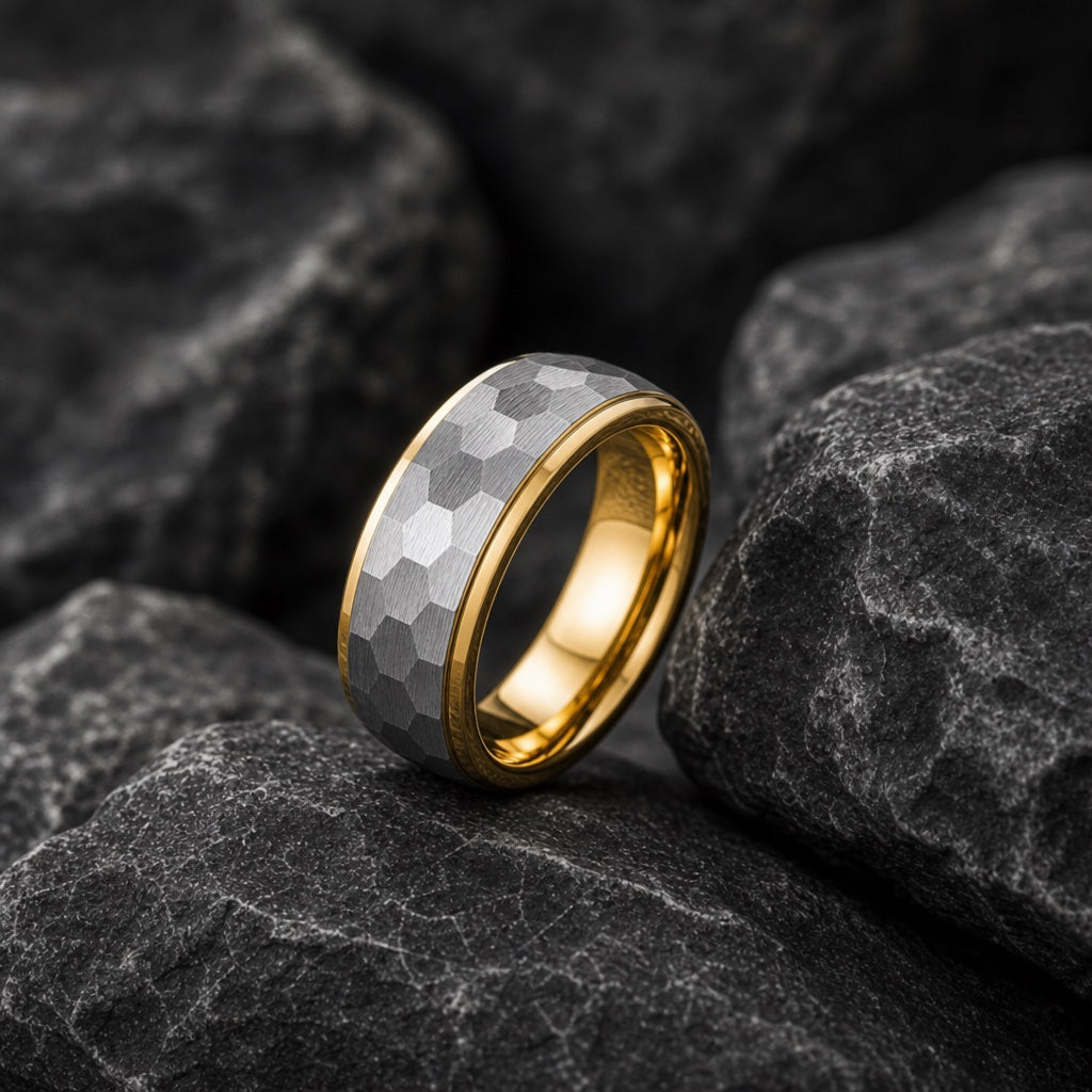 The Lustre ring resting against dark charcoal rock, hammered silver centre and yellow-gold stepped rails visible