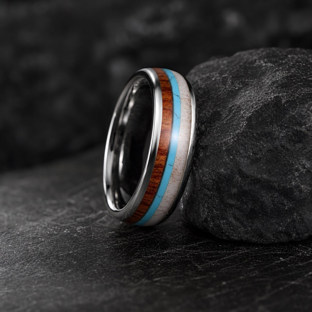 The Mana ring resting against dark charcoal rock, polished silver body and three centred inlays visible