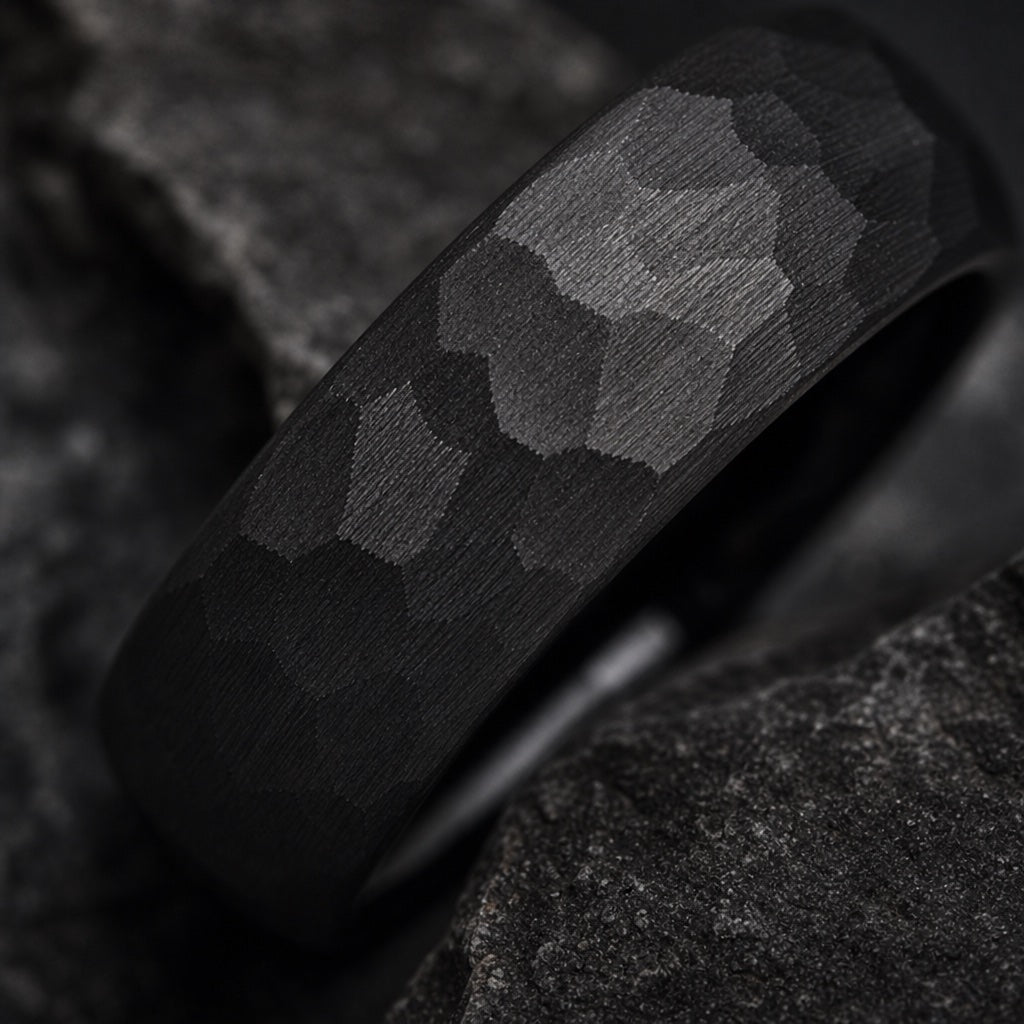 Extreme close-up of the Rugged ring's dense irregular hand-hammered matte black facets on dark charcoal stone