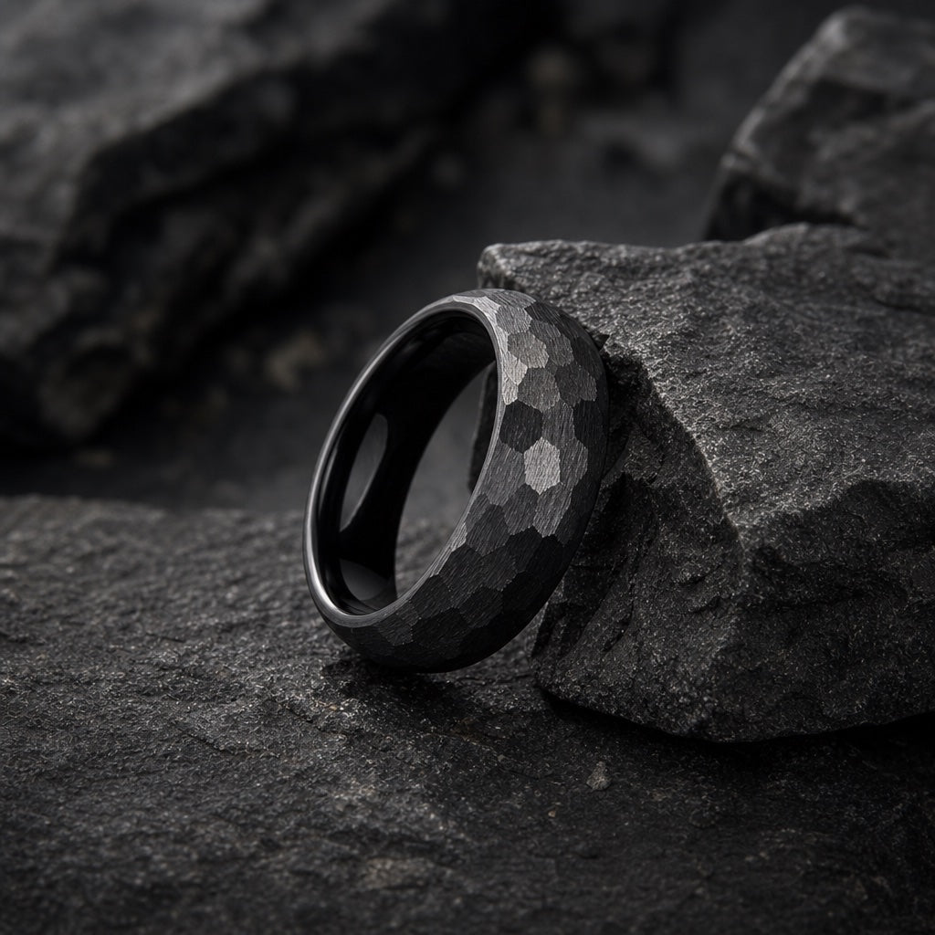 Full Rugged ring band resting on dark charcoal rock, hammered matte black exterior and round domed edge visible