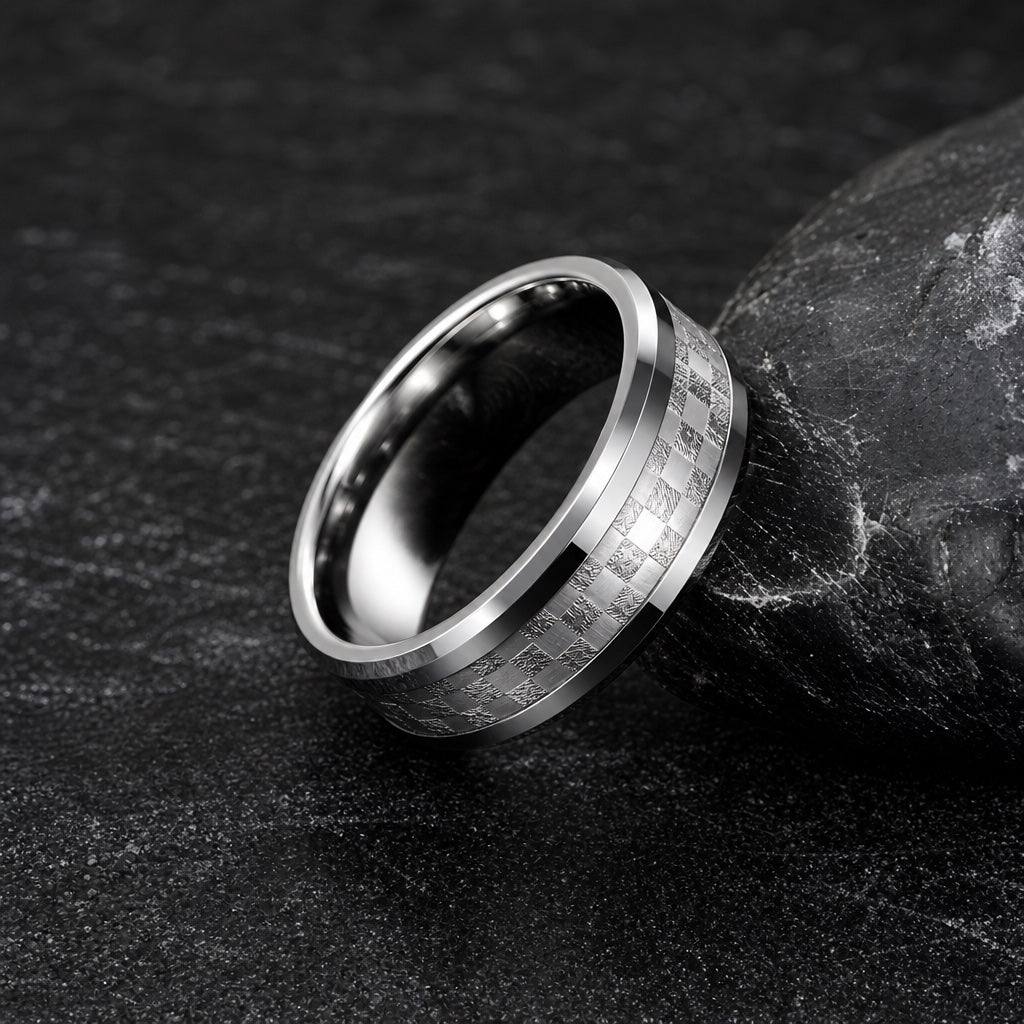 The Shimmer ring resting against dark charcoal rock, polished bevels and centred checkered silver shimmer channel visible
