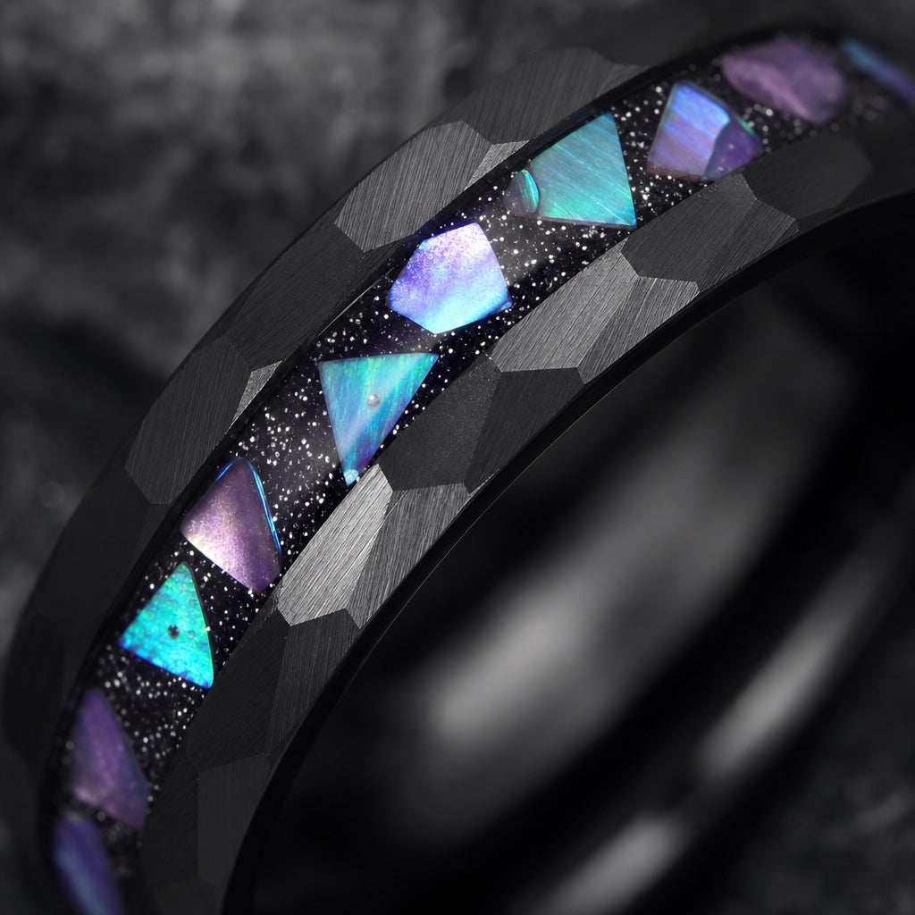 Macro of the Magus ring centred galaxy abalone inlay in black stardust resin between hammered black rails on dark charcoal stone