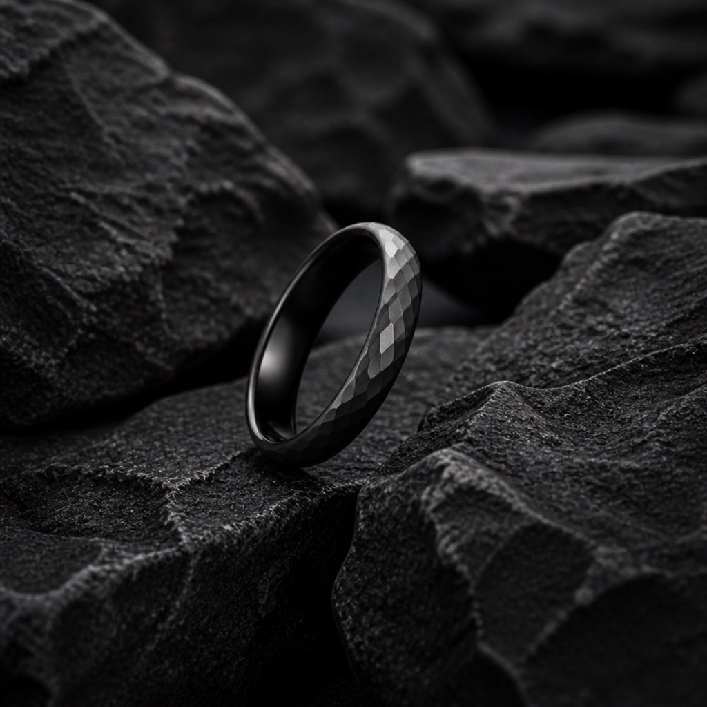 Full Marvel ring band resting on dark charcoal rock, slim hammered matte black exterior and round domed edge visible