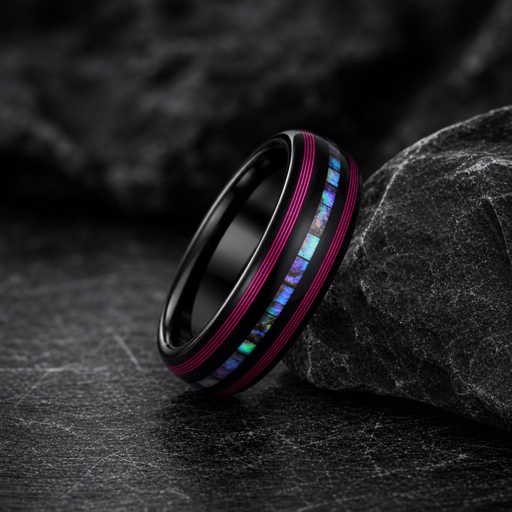 The Neon ring resting against dark charcoal rock, polished black body, neon pink rails and centred abalone visible