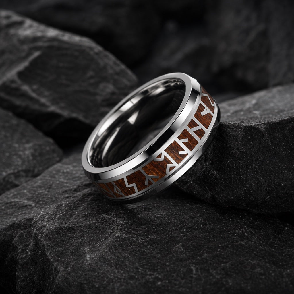 The Raider ring resting on dark charcoal stone, wood inlay and silver runes visible